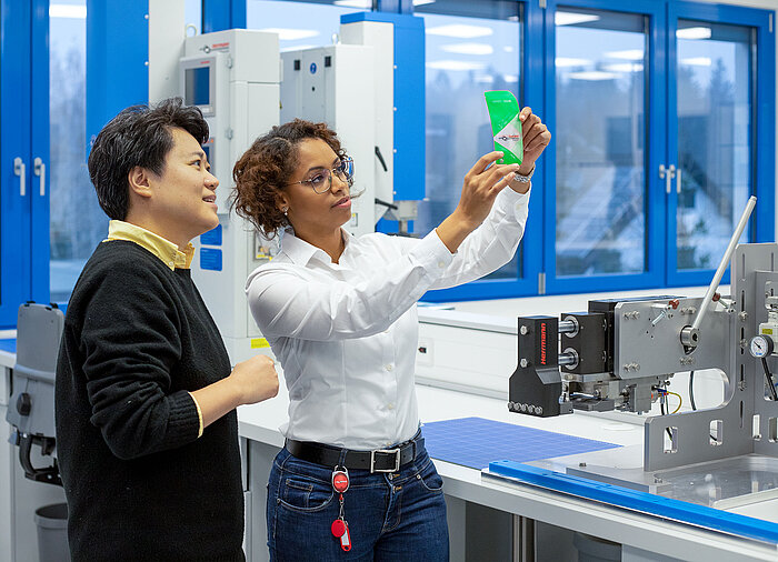 Woman shows man sealed green stand-up pouch next to Herrmann Ultrasonic sealing machine.
